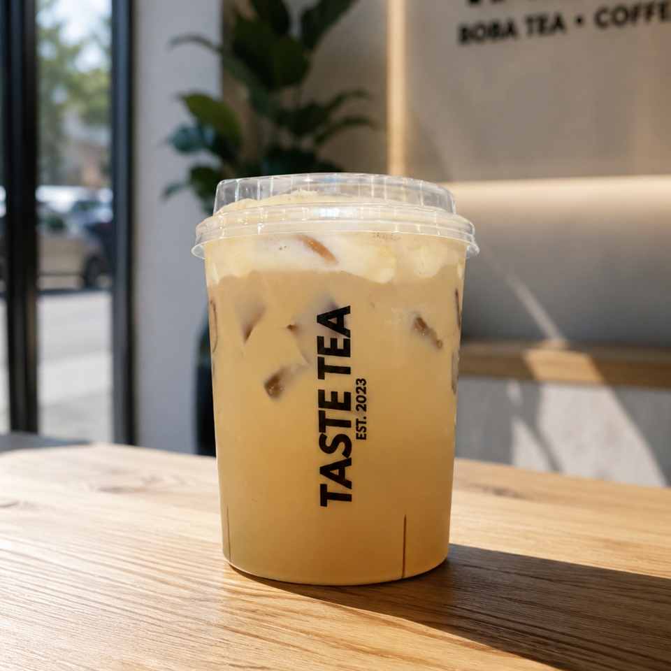 Iced milk tea in a branded Taste Tea cup sits on a wooden table inside a sunlit café.