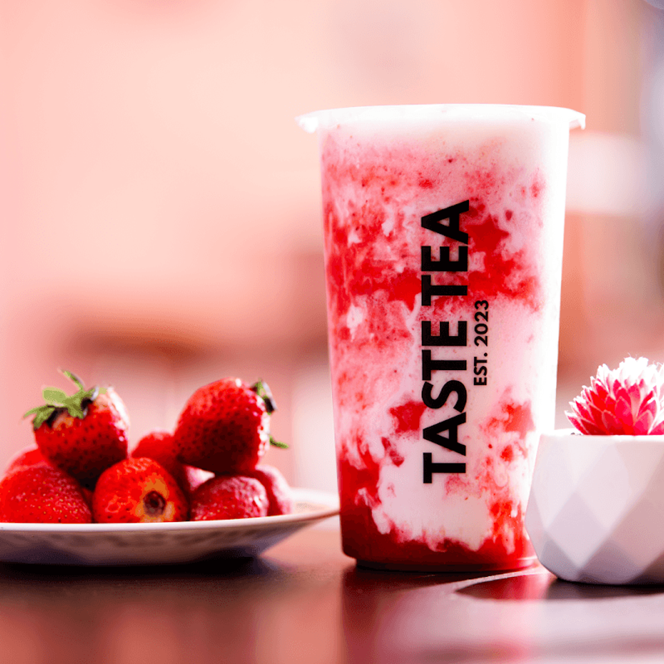 Strawberry milk tea with fresh strawberries beside a Taste Tea cup